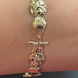 May include: Gold bracelet with a repeating pattern of seashells, sand dollars, and starfish.