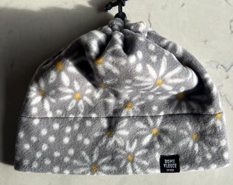May include: Gray fleece hat with a white daisy print and a yellow center. The hat has a drawstring closure and a black label that reads "Dome Fleece Est. 2022".