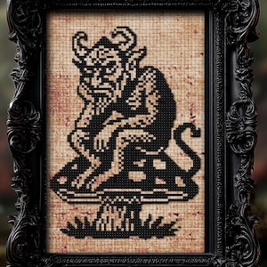 May include: A framed cross-stitch artwork featuring a black and white devil figure seated on a mushroom. The artwork is displayed in an ornate black frame. The background is a blurred forest scene with red mushrooms.