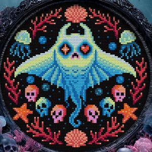 Op de afbeelding: Een ingelijst kruissteekkunstwerk met een gestileerde blauwe manta rog met hartvormige ogen, omringd door schedels, koraal en kwallen. Het kunstwerk is geplaatst tegen een donkere achtergrond met een oceaanthema, omlijst in een zwart, sierlijk frame.