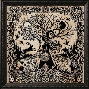 May include: Black framed cross-stitch art featuring a witchy scene with a tree, moon, and rabbit. The frame is black with silver snake and pentagram accents. Other items in the image include a cauldron, decorated eggs, and a lit candle.