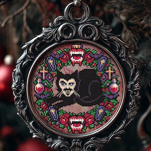 May include: A gothic-themed Christmas ornament with a cross-stitch design. The ornament features a black and silver ornate frame surrounding a circular design with a vampire motif. The design includes a vampire, roses, and other gothic elements.