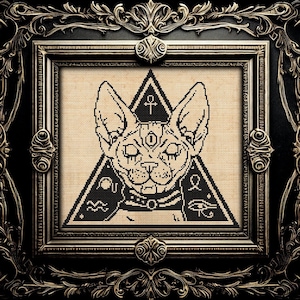 以下が含まれることがあります： アンクのシンボルが付いた首輪をしたスフィンクス猫の白黒のクロスステッチパターン。猫は目と他のシンボルのある三角形の中にいます。