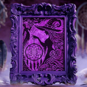 May include: A framed cross-stitch artwork in shades of purple and black. The image features a witch holding a dreamcatcher. The ornate frame is a deep purple. Feathers and a dreamcatcher are in the background, creating a mystical theme.