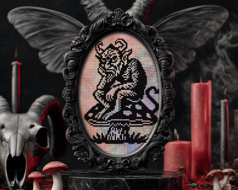 May include: A framed cross-stitch artwork featuring a black and white pixelated devil figure seated on a mushroom. The artwork is set in an ornate black oval frame. The background includes candles, a skull, and decorative wings, creating a gothic theme.