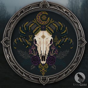 May include: A circular cross-stitch embroidery featuring a central cream-colored ram skull with large curved horns, accented by purple roses, ferns, and a crescent moon. The design includes two small occult symbols and is framed in a dark metal frame.