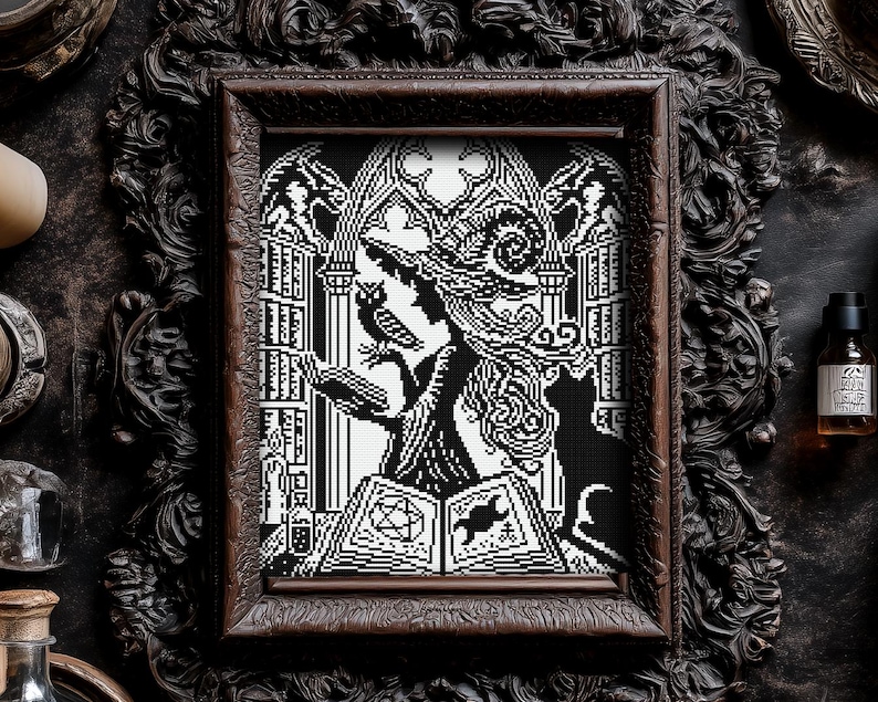 May include: Black and white cross-stitch art of a witch reading a spell book, with an owl and cat. The artwork is framed in a dark, ornate wooden frame. The witch is wearing a tall hat and is surrounded by gothic architecture.