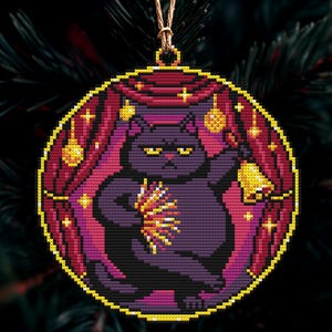 Op de afbeelding: Een ronde kerstversiering met een kruissteekontwerp van een paarse kat die een bel en een lichtuitbarsting vasthoudt. De kat staat tegen een achtergrond van rode gordijnen en gouden sterren, met een gouden rand en een ophangkoord.