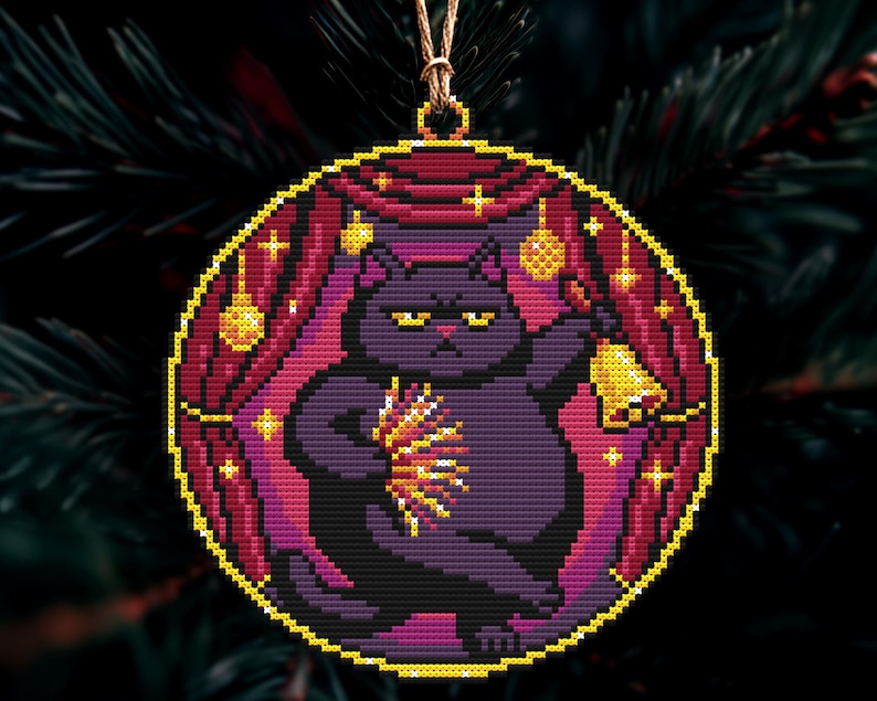 Op de afbeelding: Een ronde kerstversiering met een kruissteekontwerp van een paarse kat die een bel en een lichtuitbarsting vasthoudt. De kat staat tegen een achtergrond van rode gordijnen en gouden sterren, met een gouden rand en een ophangkoord.