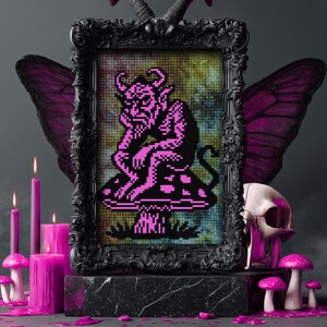 May include: A framed cross-stitch artwork featuring a pink devil figure seated on a mushroom. The black frame is adorned with decorative elements. The scene includes pink candles, mushrooms, a skull, and butterfly wings, creating a gothic aesthetic.