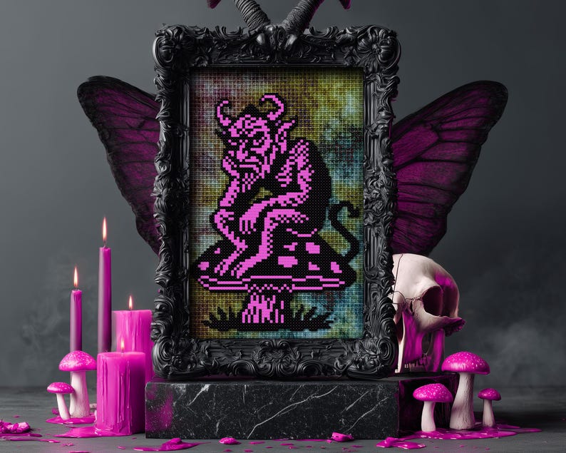May include: A framed cross-stitch artwork featuring a pink devil figure seated on a mushroom. The black frame is adorned with decorative elements. The scene includes pink candles, mushrooms, a skull, and butterfly wings, creating a gothic aesthetic.