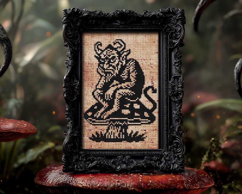 May include: A framed cross-stitch artwork featuring a black and white devil figure seated on a mushroom. The artwork is displayed in an ornate black frame. The background is a blurred forest scene with red mushrooms.