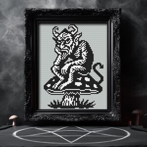May include: Black framed cross-stitch art featuring a devil figure seated on a mushroom. The artwork is in black and white, with the devil's horns, tail, and facial features clearly defined. The frame is ornate, and the background is a smoky gray.