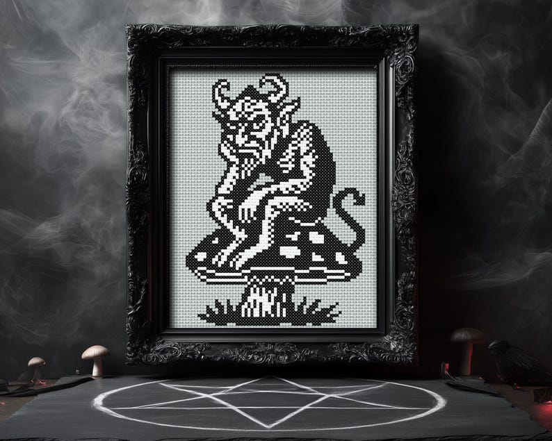May include: Black framed cross-stitch art featuring a devil figure seated on a mushroom. The artwork is in black and white, with the devil's horns, tail, and facial features clearly defined. The frame is ornate, and the background is a smoky gray.
