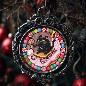Op de afbeelding: Een sierlijk zilverkleurig kerstornament met een kruissteekontwerp. De kruissteek toont een zwarte kat op een slee, omringd door kleurrijke snoepjes en lolly's. Het ornament hangt aan een zilveren ketting tegen een vage achtergrond van kerstversieringen.