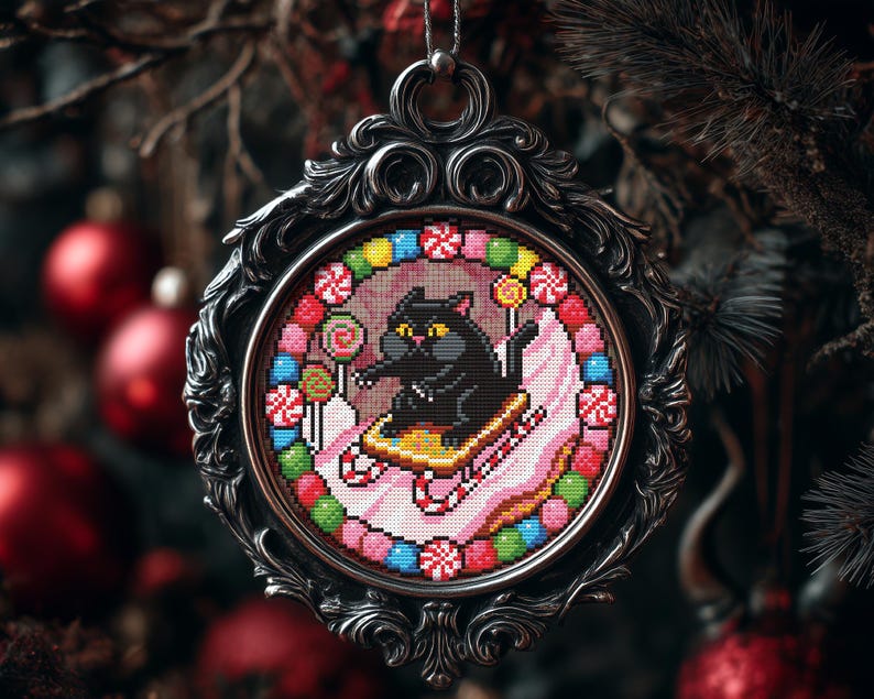 Op de afbeelding: Een sierlijk zilverkleurig kerstornament met een kruissteekontwerp. De kruissteek toont een zwarte kat op een slee, omringd door kleurrijke snoepjes en lolly's. Het ornament hangt aan een zilveren ketting tegen een vage achtergrond van kerstversieringen.