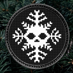 Puede incluir: Un adorno circular blanco y negro con un diseño de copo de nieve. El copo de nieve tiene una calavera en el centro.