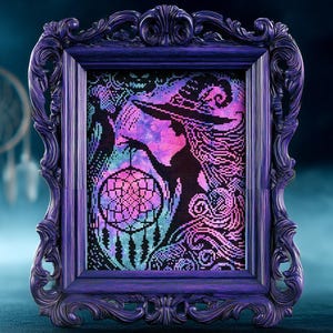 May include: A framed cross-stitch artwork featuring a witch silhouette with a dreamcatcher. The artwork uses a pixelated style with vibrant colors including pink, purple, and teal. The frame is a dark purple with ornate detailing.