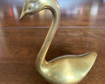 Può includere: Una statuetta di cigno in ottone dorato con un collo lungo e un corpo arrotondato.