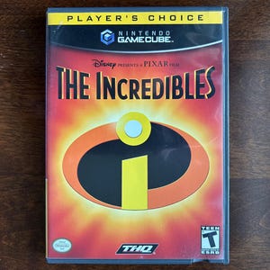 Può includere: Una custodia per videogioco Nintendo GameCube di The Incredibles, con un banner Player's Choice in alto. La copertina mostra l'iconico logo arancione e giallo su sfondo rosso, con i loghi Disney, Pixar, THQ e una classificazione ESRB Teen.