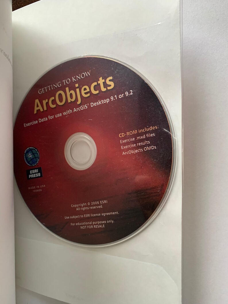 Peut inclure: Un disque CD-ROM rouge avec le texte "GETTING TO KNOW ArcObjects" et "Exercise Data for use with ArcGIS Desktop 9.1 or 9.2". Le disque comprend &eacute;galement le texte "CD-ROM includes: Exercise.mxd files Exercise, results ArcObjects OMDS".