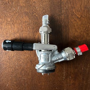 May include: A silver beer tap with a black handle and a red cap. The tap features a lever and multiple connection points. The text "PAT. PENDING" and "MICRO MATIC" are visible on the tap.