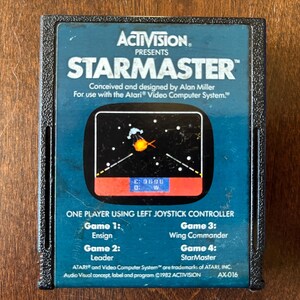 May include: A black Atari game cartridge for the game StarMaster. The cartridge has a blue label with white text and a small screen shot of the game. The text on the label reads "ACTIVISION PRESENTS STARMASTER Conceived and designed by Alan Miller For use with the Atari Video Computer System." The text at the bottom of the label reads "ATARI and Video Computer System are trademarks of ATARI, INC. Audio Visual concept, label and program ©1982 ACTIVISION AX-016".
