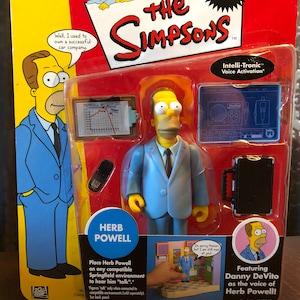 May include: A plastic action figure of Herb Powell from The Simpsons, wearing a blue suit and a yellow tie. The figure is packaged in a colorful box with the show's logo and the text "Intelli-Tronic Voice Activation".