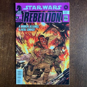 May include: A Star Wars Rebellion comic book. The cover features a dynamic illustration of two figures in a fiery battle scene. The title "REBELLION" is prominently displayed, along with the text "A BROKEN ALLIANCE, A FATAL CHOICE!"