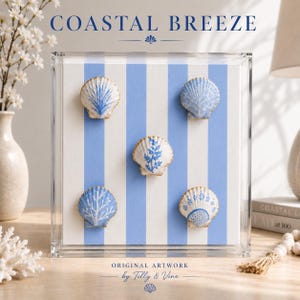 May include: A square acrylic display case containing a white and light blue striped background with five decorative seashells attached. Each shell features a unique blue painted botanical or coral pattern. The text COASTAL BREEZE and ORIGINAL ARTWORK by Tilly & Vine is printed on the front of the clear case.