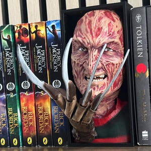 May include: A bookshelf display with a Freddy Krueger bust and metal claws, alongside fantasy novels. The books include the Percy Jackson series and The Lord of the Rings trilogy, creating a horror and fantasy theme.