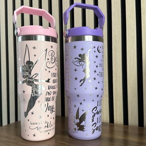 May include: Two stainless steel tumblers with pink and purple lids and handles. The tumblers have a silver glitter finish and feature a Tinkerbell silhouette with inspirational quotes. The pink tumbler says "All you need is trust and a little bit of pixie dust. Believe in a little bit of magic. Leave a little sparkle wherever you go." The purple tumbler says "Believe in a little bit of magic. If you can dream it, you can do it. The best is yet to come. A little sweet, a little sass."
