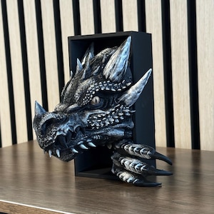 May include: A black and silver dragon head sculpture mounted on a black wooden frame. The dragon's eyes are open and its mouth is slightly open. The sculpture is a 3D design and appears to be made of resin.