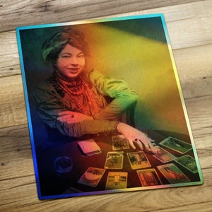 May include: A woman with dark hair and a red necklace sits at a table with a crystal ball and tarot cards spread out in front of her. The image is in a vintage style with a rainbow overlay.