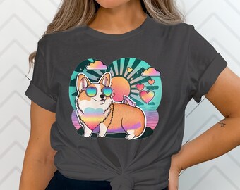 May include: A dark grey t-shirt featuring a colourful illustration of a corgi wearing sunglasses and a rainbow bandana. The corgi is standing on a beach with a sunset and hearts in the background.