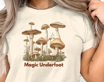 May include: A white t-shirt with a graphic of brown mushrooms and the text "Magic Underfoot" in brown.