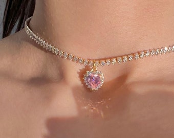 May include: A gold choker necklace with a pink heart pendant encrusted with clear rhinestones.