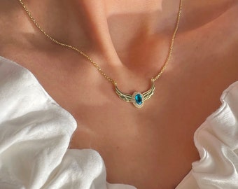 May include: A gold chain necklace with a blue gemstone pendant. The pendant is shaped like a pair of wings with a round gemstone in the center.