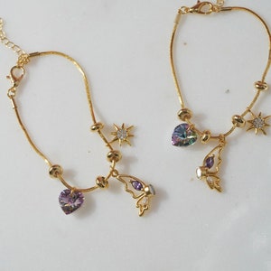 May include: Two gold chain bracelets with charms. One bracelet has a purple heart charm, a butterfly charm, and a star charm. The other bracelet has a rainbow heart charm, a butterfly charm, and a star charm.
