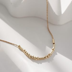 May include: A gold necklace with a delicate chain and alternating round and cylindrical beads.