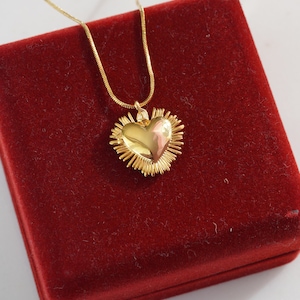 May include: A gold heart-shaped pendant necklace with a textured design, displayed in a red velvet box.