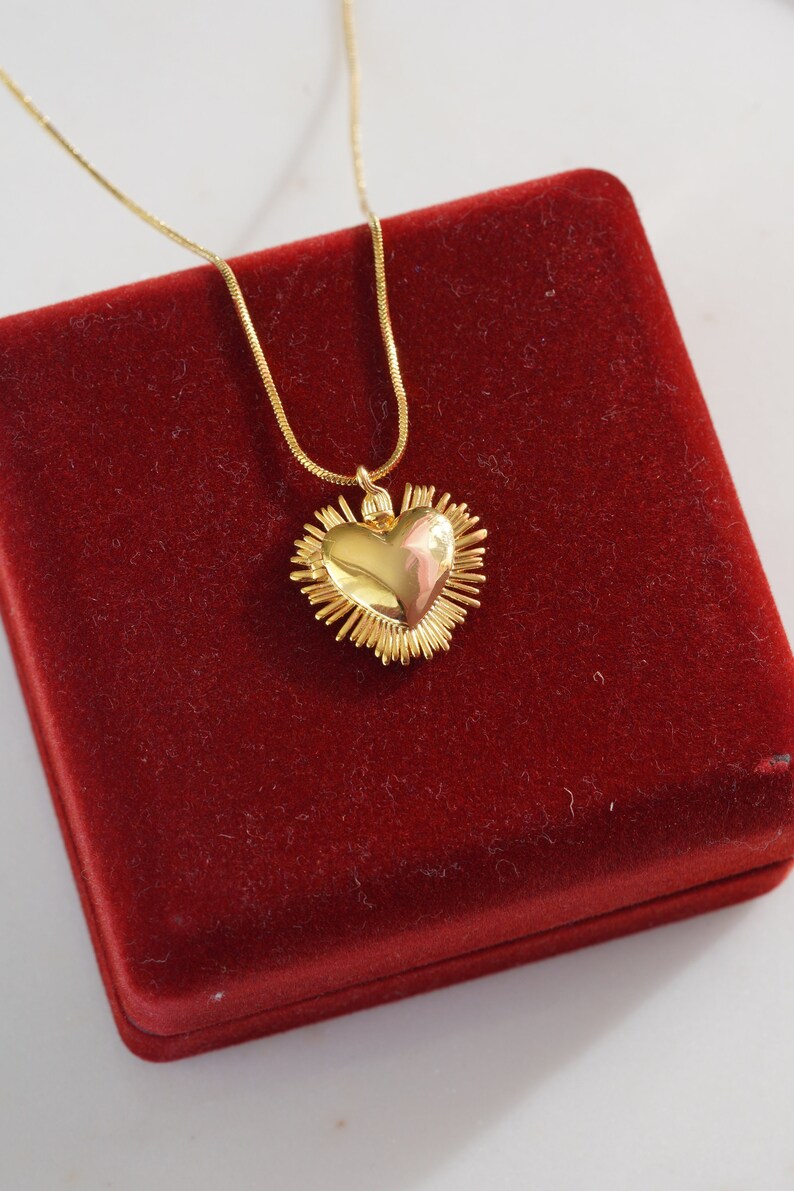 May include: A gold heart-shaped pendant necklace with a textured design, displayed in a red velvet box.