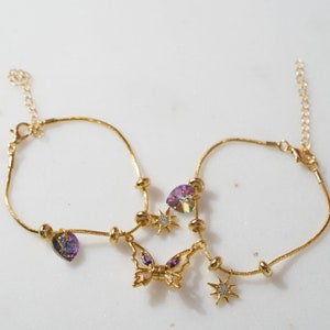 May include: Two gold anklets with purple and clear crystal charms, including a butterfly charm and star charms.