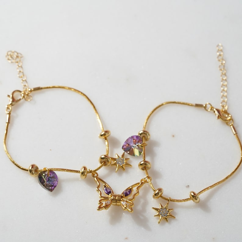 May include: Two gold anklets with purple and clear crystal charms, including a butterfly charm and star charms.