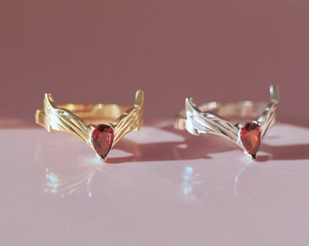 May include: Two rings with a red gemstone in the center. The ring on the left is gold and the ring on the right is silver.