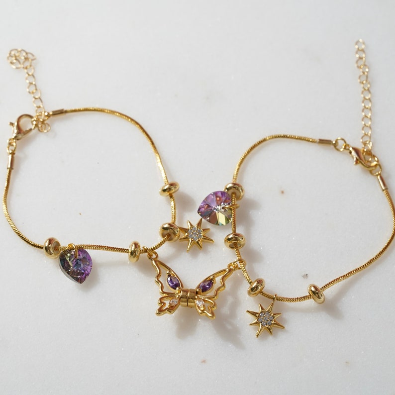 May include: Gold anklet with a butterfly charm, heart charms, and star charms. The charms are decorated with purple and clear crystals.