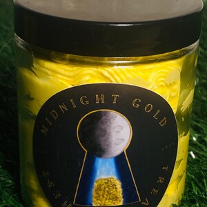 Op de afbeelding: Een gele pot met een zwart deksel en een zwart en gouden etiket met de tekst "Midnight Gold Treasure Chest". Het etiket heeft een sleutelgat met een maan en een goudklompje erin.