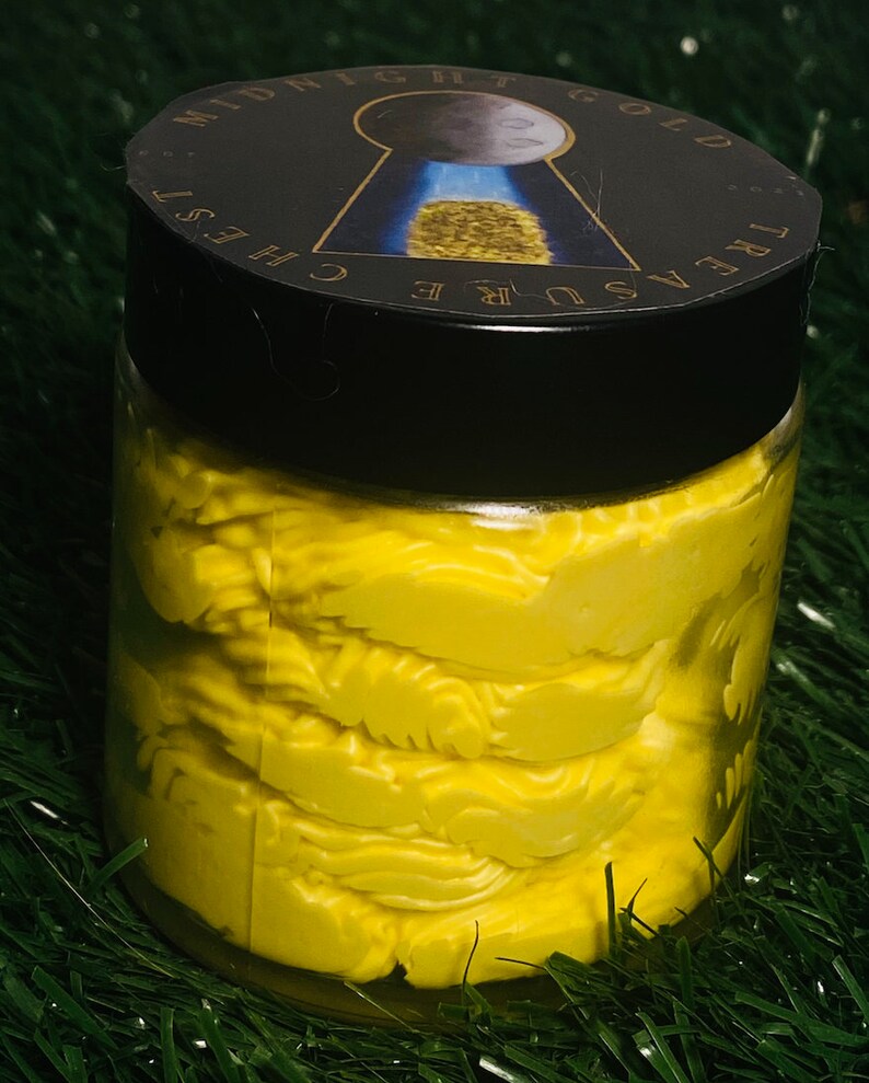 Op de afbeelding: Een glazen pot gevuld met een heldergele, getextureerde, romige substantie. De pot heeft een zwarte deksel met een gouden sticker waarop "Treasure Chest Midnight Gold" staat.