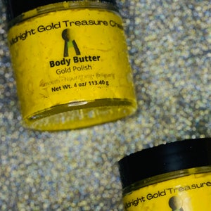 Op de afbeelding: Twee gele potten met body butter en zwarte deksels. De potten zijn gelabeld met "Midnight Gold Treasure" en "Body Butter Gold Polish". De potten staan op een glinsterende achtergrond.