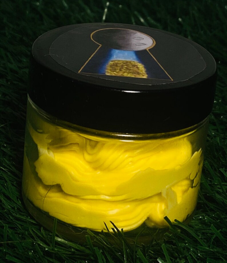 Op de afbeelding: Een gele pot met een zwart deksel. Het deksel heeft een sticker met een sleutelgat en een maan. De pot is gevuld met een gele substantie.